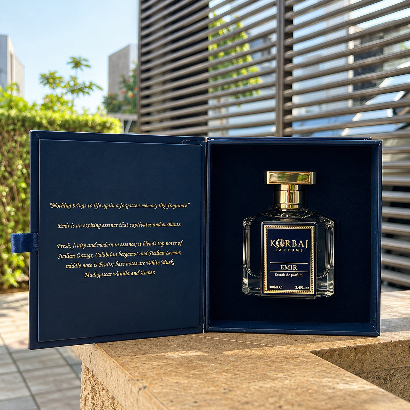 Korbaj Emir 100ml unisex citrus perfume: bottle inside an open navy presentation box on a sunlit table.