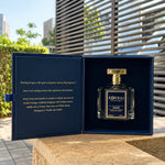 Korbaj Emir 100ml unisex citrus perfume: bottle inside an open navy presentation box on a sunlit table.