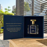 Korbaj Emir 100ml unisex citrus perfume: bottle inside an open navy presentation box on a sunlit table.